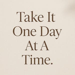 May include: A minimalist design featuring the text "Take It One Day At A Time" in a brown serif font. The text is centered on a beige background, creating a simple and motivational aesthetic.