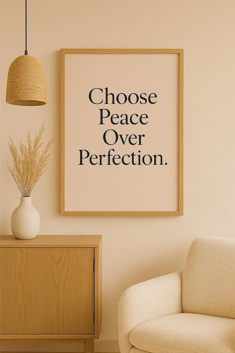 May include: A framed print with the text "Choose Peace Over Perfection" in a minimalist style. The artwork is displayed in a room with a neutral color palette, featuring a wooden cabinet, a beige armchair, and a woven pendant light.