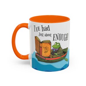 May include: White ceramic mug with an orange interior and handle. The mug features a whimsical illustration of a frog in a boat with an open book. Text on the mug reads "I've had Just about ENOUGH!"