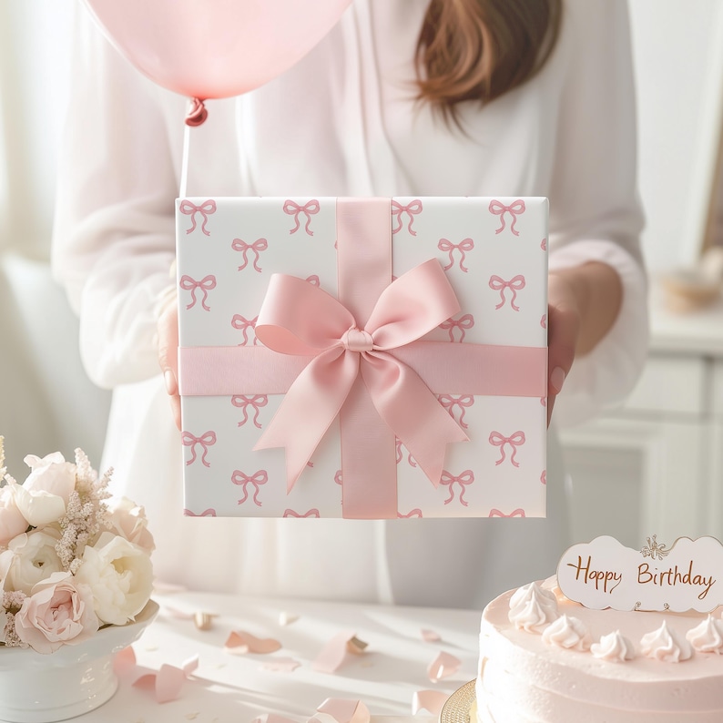 May include: A wrapped gift box with a pink bow and ribbon. The box is white with a pattern of pink bows. A pink balloon is held above the box. A cake with a "Happy Birthday" sign is in the background.