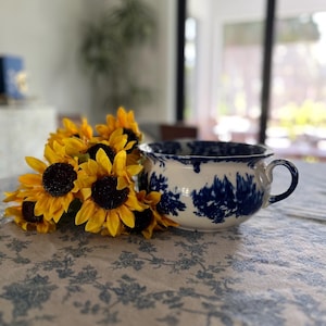 Puede incluir: Un tazón de cerámica blanco con un patrón floral azul y blanco. El tazón está lleno de un ramo de girasoles amarillos.