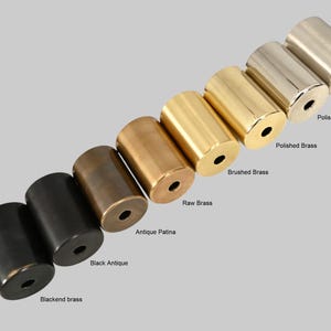 May include: A row of eight metal cylinders in different finishes, including blackend brass, black antique, antique patina, raw brass, brushed brass, polished brass, brushed chrome, and polished chrome.
