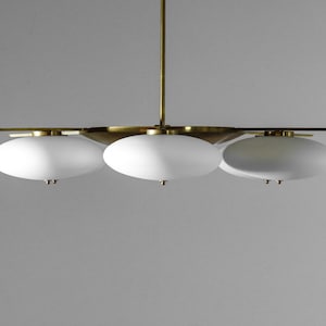 May include: A brass and white glass chandelier with three oval-shaped lights.