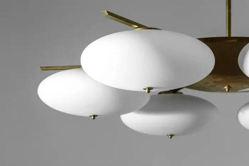 May include: A brass and white glass chandelier with multiple round, white glass shades. The chandelier has a modern design and is suspended from the ceiling.
