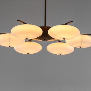 May include: A six-light chandelier with a bronze finish and white frosted glass shades. The shades are shaped like rounded ovals and are arranged in a circular pattern around the central fixture.