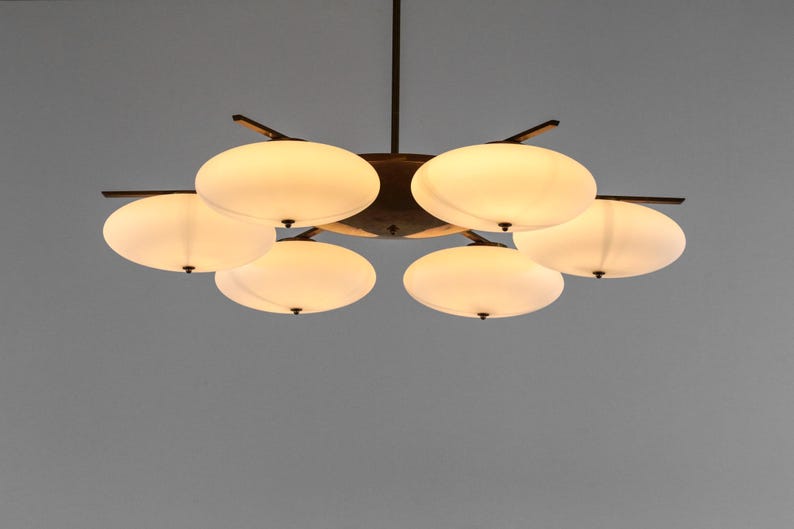 May include: A six-light chandelier with a bronze finish and white frosted glass shades. The shades are shaped like rounded ovals and are arranged in a circular pattern around the central fixture.