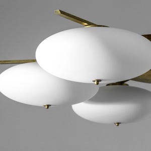 May include: A brass and white glass chandelier with multiple round, white glass shades. The chandelier has a modern design with a central brass plate and multiple arms extending out to the shades.