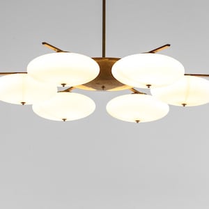 May include: A brass and white glass chandelier with six lights. The chandelier has a starburst design with five arms and six round, white glass shades.