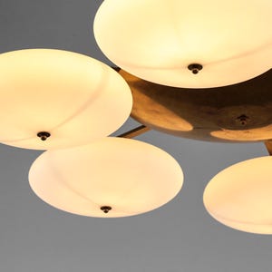 May include: A brass ceiling light fixture with five white frosted glass shades. The shades are round and have a slight curve to them. The fixture has a modern design.