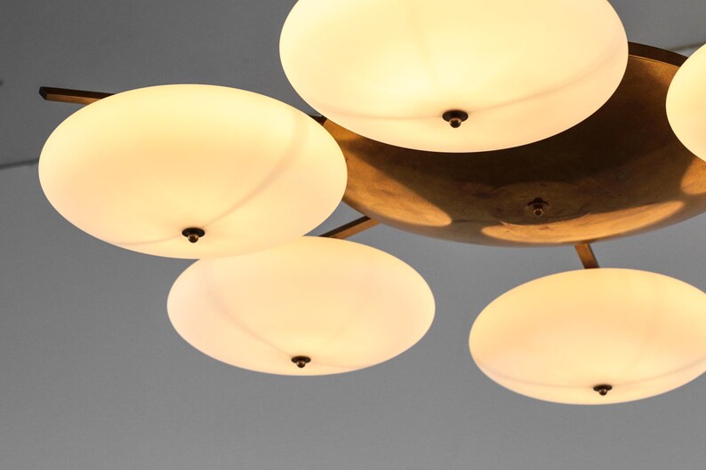 May include: A brass ceiling light fixture with five white frosted glass shades. The shades are round and have a slight curve to them. The fixture has a modern design.