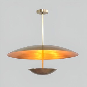 May include: A brass pendant light with a large, round, flat shade and a smaller, round, bowl-shaped shade hanging below it.