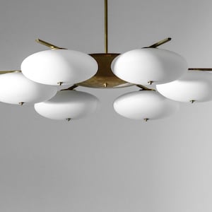 May include: A brass and white glass chandelier with six lights. The chandelier has a circular base and six arms that extend out to hold the lights. The lights are white glass globes.