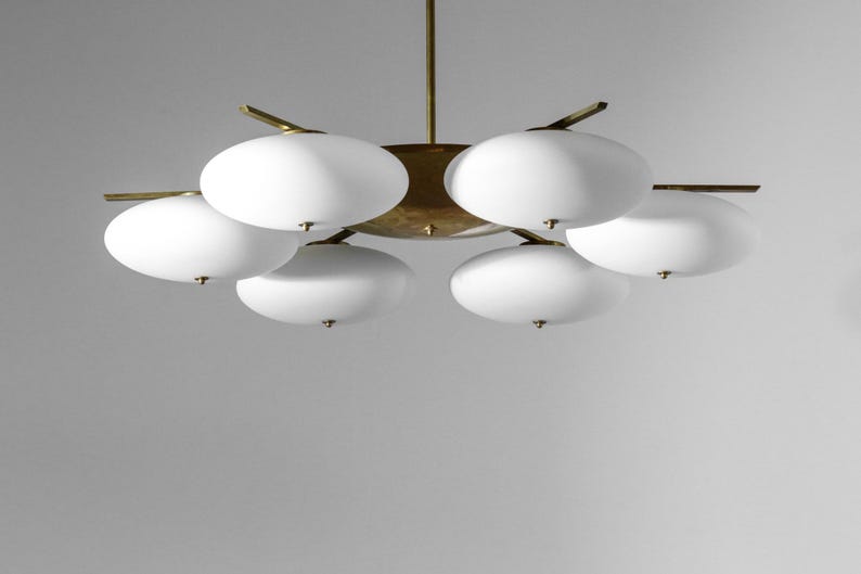 May include: A brass and white glass chandelier with six lights. The chandelier has a circular base and six arms that extend out to hold the lights. The lights are white glass globes.