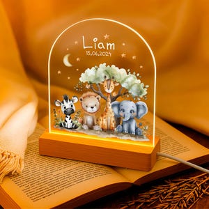 Peut inclure: Une veilleuse en bois avec un dôme en acrylique transparent représentant une illustration aquarelle d'une girafe, d'un zèbre, d'un éléphant et d'un lion dans un décor de jungle. Le dôme comprend également le nom "Liam" et la date "15.06.2024".