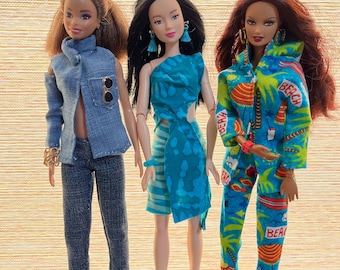 May include: Three fashion dolls are displayed, each in a unique outfit. The first doll wears a denim jacket and pants. The second doll is in a turquoise dress. The third doll is in a blue and green beach-themed jumpsuit. All dolls have different hairstyles and accessories.