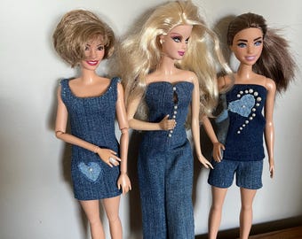 May include: Three fashion dolls wearing denim outfits. The left doll has short blonde hair and a blue denim dress with a heart patch. The center doll has long blonde hair and a blue denim jumpsuit. The right doll has brown hair and a blue denim top with a heart-shaped pearl design and matching shorts.