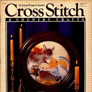 May include: A vintage magazine cover for "Cross Stitch & Country Crafts" featuring a framed cross-stitch design of a donkey and figures, dated 1988. The cover includes lit candles, a Bible, and the text "36 Great Projects Inside!"