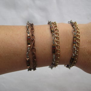 May include: Three layered bracelets with copper, silver, and gold chain links. Each bracelet features brown and red resistor beads.