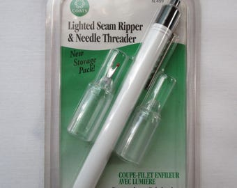 May include: A white Coats Lighted Seam Ripper & Needle Threader in a plastic blister pack. The set includes a white pen-style handle with a black top, two clear protective caps, and a seam ripper attachment. Text reads: New Storage Pack!