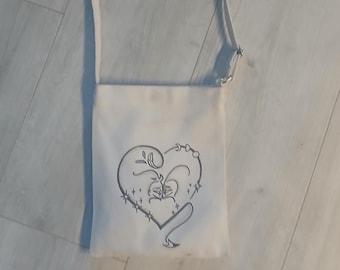 Peut inclure: Un sac à bandoulière en toile blanche avec un motif de cœur noir et blanc. Le cœur a un motif floral et un ruban.