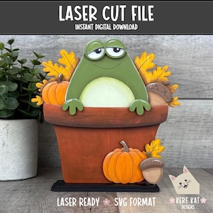 May include: A laser-cut file featuring a whimsical frog in a flower pot, surrounded by pumpkins, acorns, and fall leaves. The frog is green with a white belly, and the pot is a warm terracotta color. Text on the image reads "LASER CUT FILE" and "INSTANT DIGITAL DOWNLOAD."