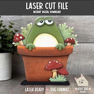Pode incluir: Um arquivo de corte a laser de um sapo caprichoso em um vaso de flores, com detalhes de cogumelos vermelhos e brancos. O sapo é verde com a barriga branca, e o vaso é cor de terracota. O texto diz "LASER CUT FILE" e "INSTANT DIGITAL DOWNLOAD".