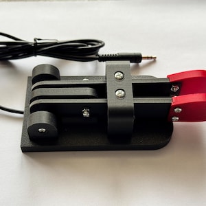 Può includere: Un pedale per piedi nero con due pulsanti rossi e un cavo nero con un jack da 3,5 mm.