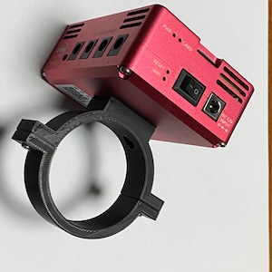Può includere: Un dispositivo rosso con una staffa di montaggio nera. Il dispositivo ha un pulsante di accensione, uno slot per schede e un ingresso DC 12V. Il dispositivo è etichettato "PWR CARD" e "DC 12V INPUT".
