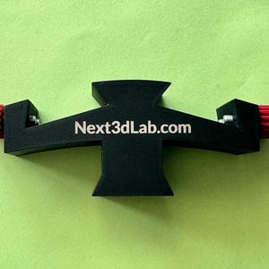 Op de afbeelding: Zwart plastic 3D-printer accessoire met twee rode knoppen en de tekst "Next3DLab.com" gedrukt op de voorkant.
