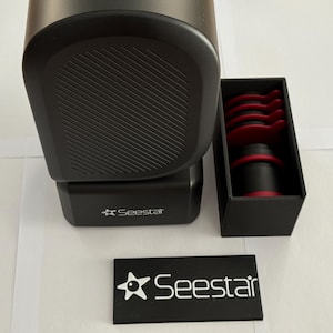 Può includere: Un macinacaffè elettrico nero SeeStar con un contenitore rimovibile per i fondi di caffè. Il macinacaffè è accanto a una scatola nera con accenti rossi che contiene un set di filtri per caffè.