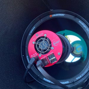 Può includere: Primo piano di un telescopio Schmidt-Cassegrain Celestron StarBright XLT da 8 pollici (203 mm) f/2.0 con una fotocamera rosa compatibile con ASCOM. La fotocamera ha una porta USB 2.0 out e una porta USB 3.0 in.