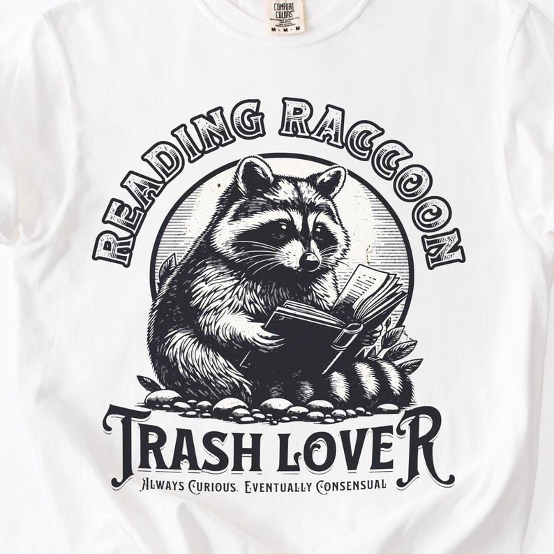 Puede incluir: Camiseta blanca con una ilustraci&oacute;n en blanco y negro de un mapache leyendo un libro. El texto "READING RACCOON" est&aacute; arqueado sobre el mapache, y "TRASH LOVER" est&aacute; debajo. Tambi&eacute;n se incluye la frase "ALWAYS CURIOUS. EVENTUALLY CONSENSUAL".