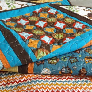 May include: A multi-layered quilt with a blue, brown, orange and white pattern. The quilt features a variety of geometric shapes and designs, including owls, leaves and zigzags.