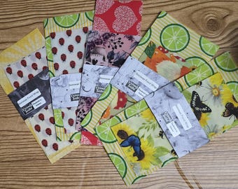 May include: Assortment of colorful beeswax food wraps with various designs, including ladybugs, flowers, and limes. Each wrap has a label that reads "Beeswax Food Wrap Handmade in Tasmania".
