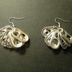 May include: A pair of handmade silver earrings. Each earring features a cluster of recycled aluminum can pull tabs, suspended from a silver hook. The earrings have a unique, upcycled aesthetic.
