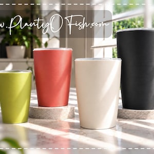 May include: Four cylindrical tumblers in lime green, coral, cream, and black, each featuring a simple rim and smooth finish. The text www.PlantyOFish.com is displayed at the top of the image. These vessels are arranged in a row, showcasing their varying heights and solid colors.