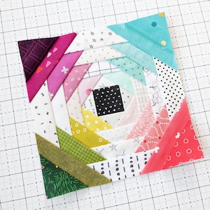 Könnte beinhalten: Ein farbenfroher Patchwork-Quiltblock mit einem Spiraldesign. Der Block besteht aus verschiedenen Stoffen mit unterschiedlichen Mustern, darunter Punkte, Sterne und geometrische Formen. Der Block ist vor einem weißen Gitterhintergrund platziert.