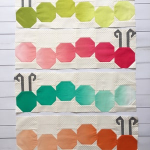 Op de afbeelding: Vier rijen van stoffen patchwork die aan elkaar zijn genaaid om een ​​rupsontwerp te cre&euml;ren. De rups is gemaakt van verschillende tinten groen, roze, turquoise en oranje stof. Elke rij heeft een ander kleurenschema.