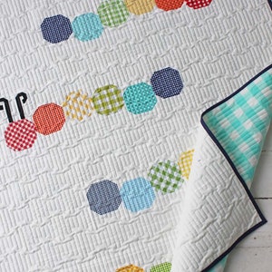 Op de afbeelding: Een wit babydekbed met een kleurrijk rupsontwerp. De rups is gemaakt van achteckige stofstukken in tinten rood, oranje, geel, groen, blauw en wit. Het dekbed heeft een witte achtergrond met een subtiel gestikt patroon.