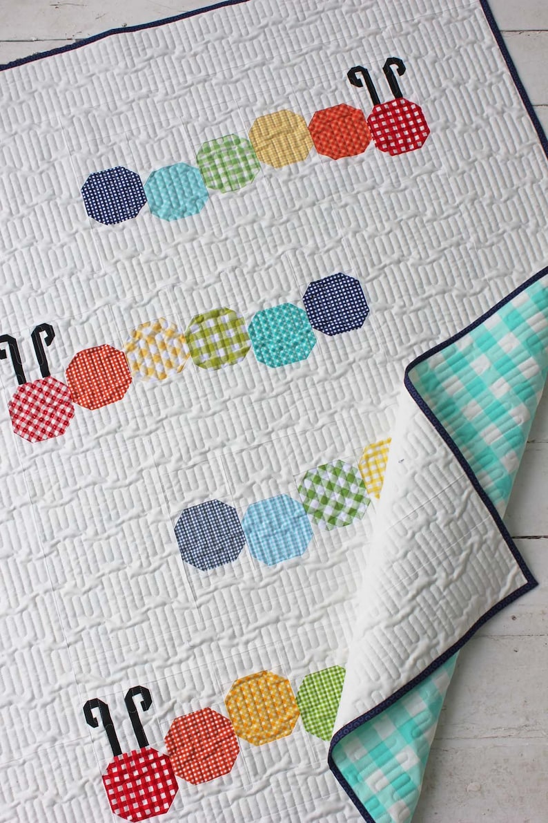 Op de afbeelding: Een wit babydekbed met een kleurrijk rupsontwerp. De rups is gemaakt van achteckige stofstukken in tinten rood, oranje, geel, groen, blauw en wit. Het dekbed heeft een witte achtergrond met een subtiel gestikt patroon.
