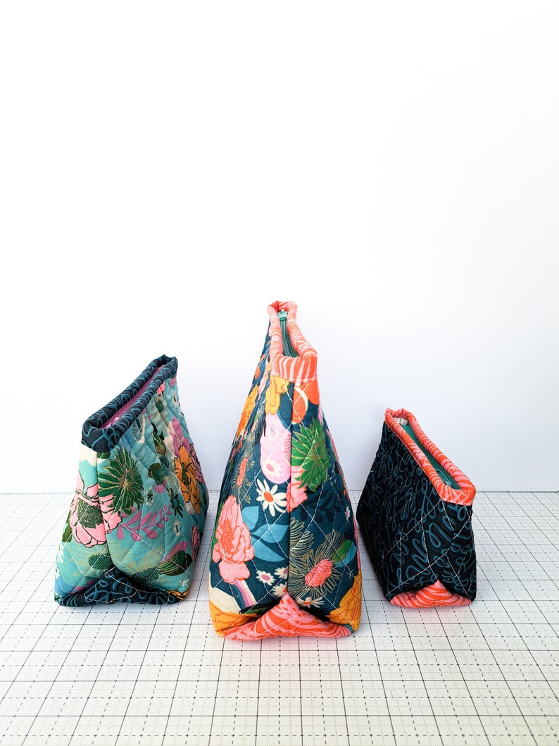 May include: Three quilted fabric zippered pouches in different sizes. The largest pouch is teal with a floral pattern, the medium pouch is black with a script pattern, and the smallest pouch is teal with a floral pattern.