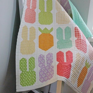May include: A white quilt with a patchwork design featuring bunnies, carrots, and pineapples. The quilt is made with a variety of colorful fabrics, including pink, green, yellow, orange, and purple.