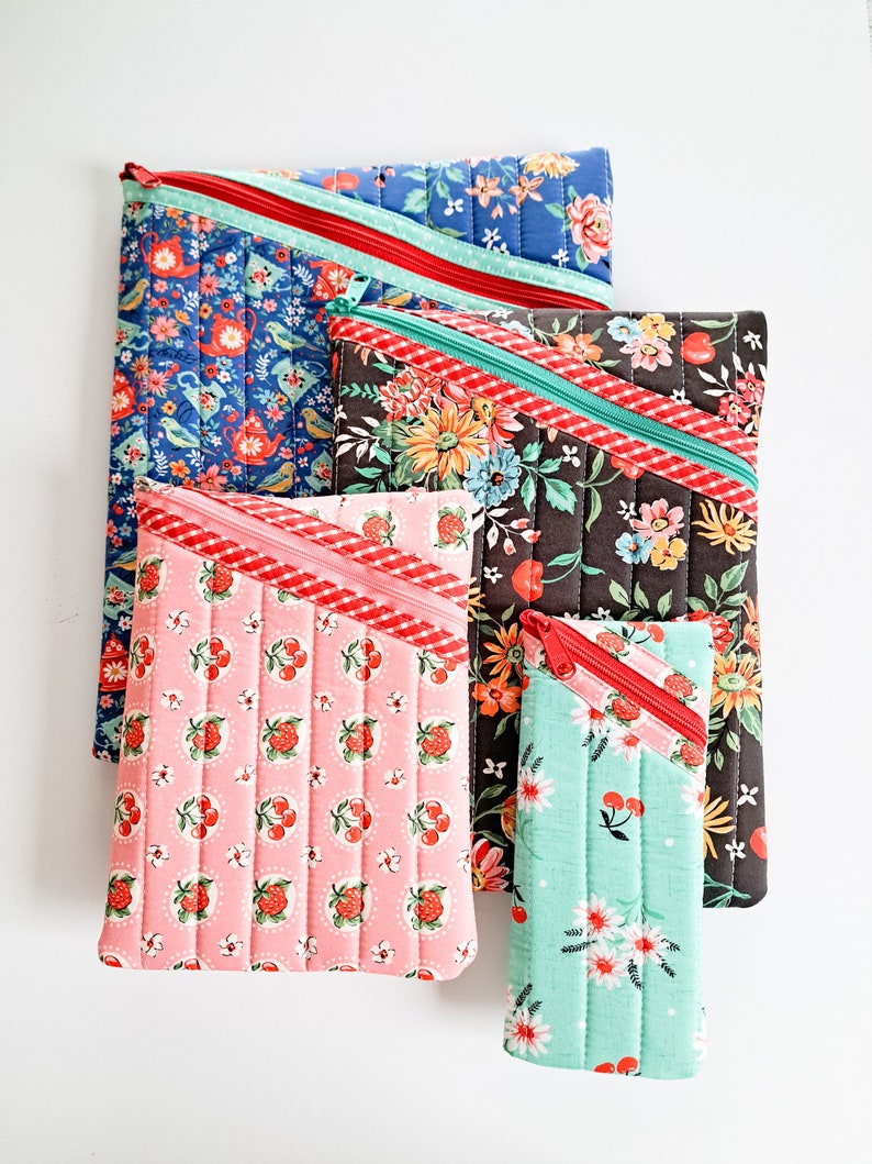 May include: Five quilted zippered pouches in various floral patterns. The pouches are arranged in a stack, with the largest pouch at the top and the smallest pouch at the bottom. The pouches are made of cotton fabric and have a red zipper.