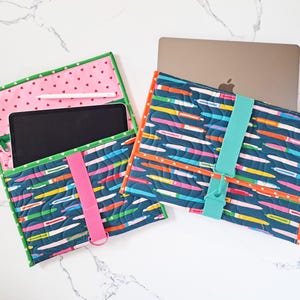Könnte beinhalten: Zwei gesteppte Laptop- und Tablet-Hüllen. Eine Hülle ist geöffnet und zeigt ein Tablet und einen rosa Innenraum mit Herzmuster. Die andere Hülle enthält einen Laptop. Beide Hüllen haben ein blaues Stiftmuster und farbige Akzente.