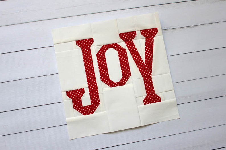 May include: A white fabric square with the word "JOY" in red with white polka dots.