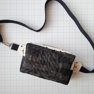 May include: A black quilted fabric bag with a white star pattern and a black strap. The bag has a zipper closure and a small pocket on the front.
