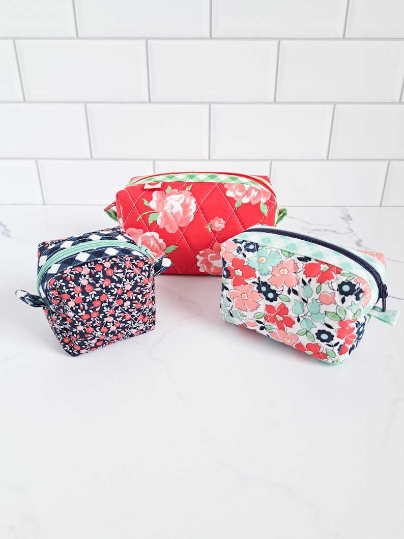 May include: Three quilted zippered pouches in different floral patterns. The largest pouch is red with pink roses, the medium pouch is white with pink and blue flowers, and the smallest pouch is blue with pink and white flowers.