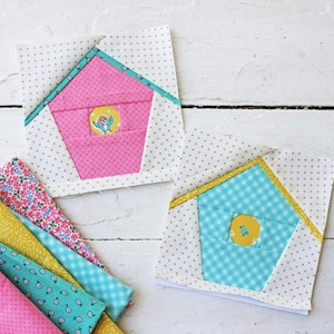May include: Two unfinished quilt blocks featuring a birdhouse design. The first block has a pink birdhouse with a blue bird and a white background. The second block has a blue and white checkered birdhouse with a yellow bird and a white background.