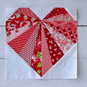 May include: A red and pink heart-shaped quilt block made with various patterned fabrics. The block is made up of 12 triangles, each with a different pattern. The block is surrounded by a white background.