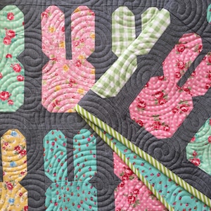 May include: A quilt with a patchwork design featuring bunny shapes in various floral prints. The quilt is made with a gray background and a green and white gingham border.